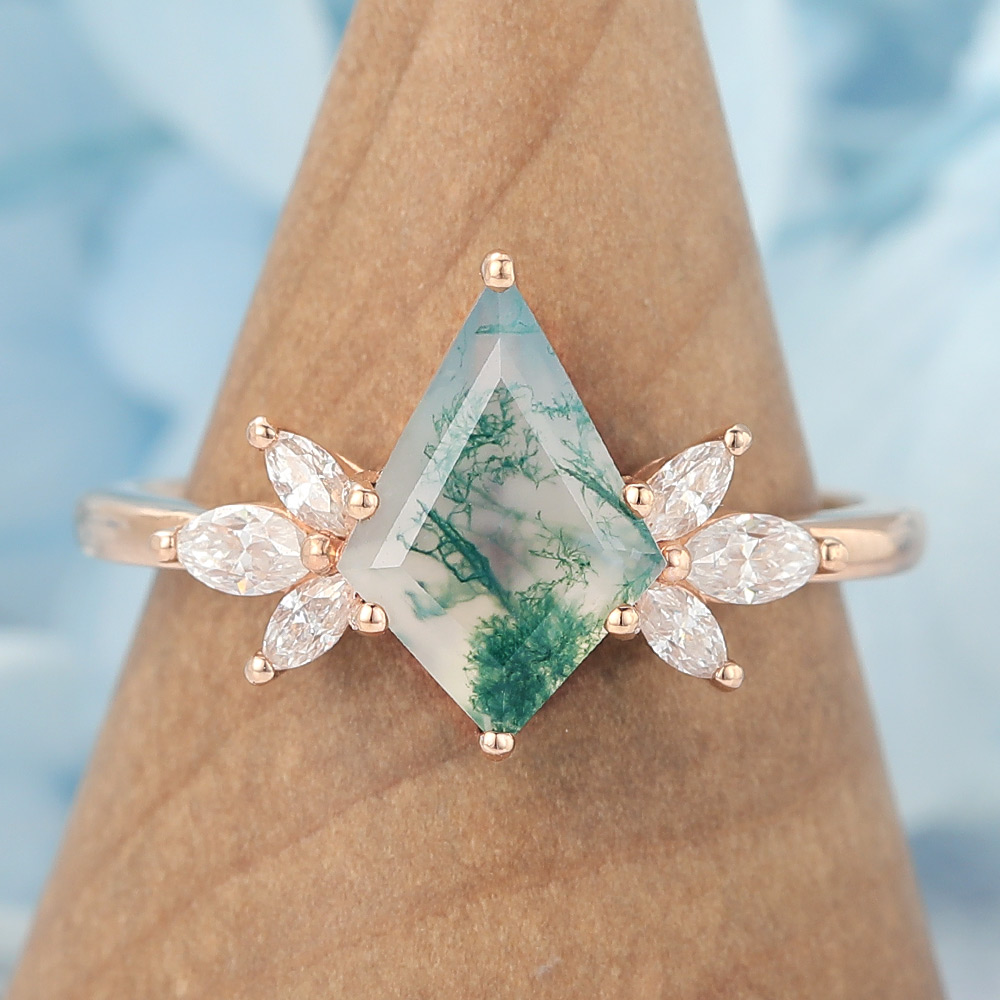 This nature-inspired engagement ring features a striking kite cut moss agate as the center stone, surrounded by a graceful cluster of marquise-cut accents that mimic the look of blooming petals or leaves. The rich, earthy patterns of moss agate make each ring truly one of a kind, while the marquise details add sparkle and movement.