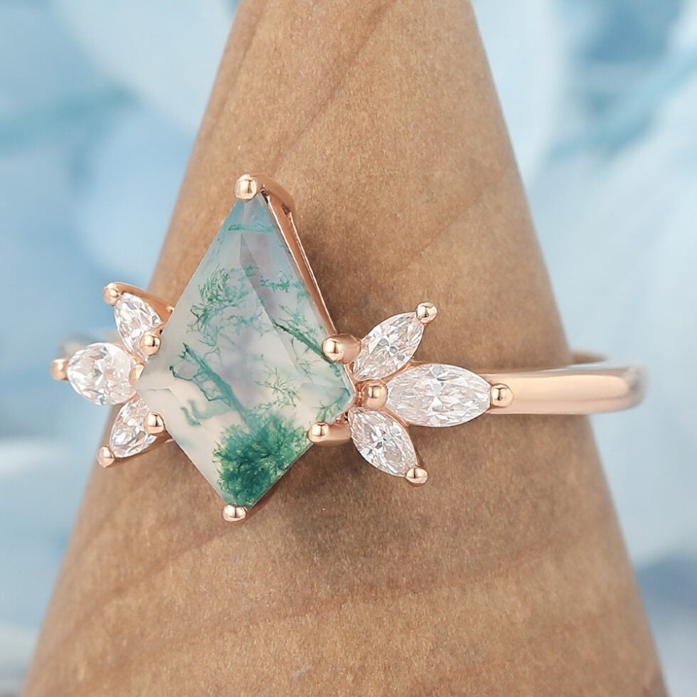 This nature-inspired engagement ring features a striking kite cut moss agate as the center stone, surrounded by a graceful cluster of marquise-cut accents that mimic the look of blooming petals or leaves. The rich, earthy patterns of moss agate make each ring truly one of a kind, while the marquise details add sparkle and movement.