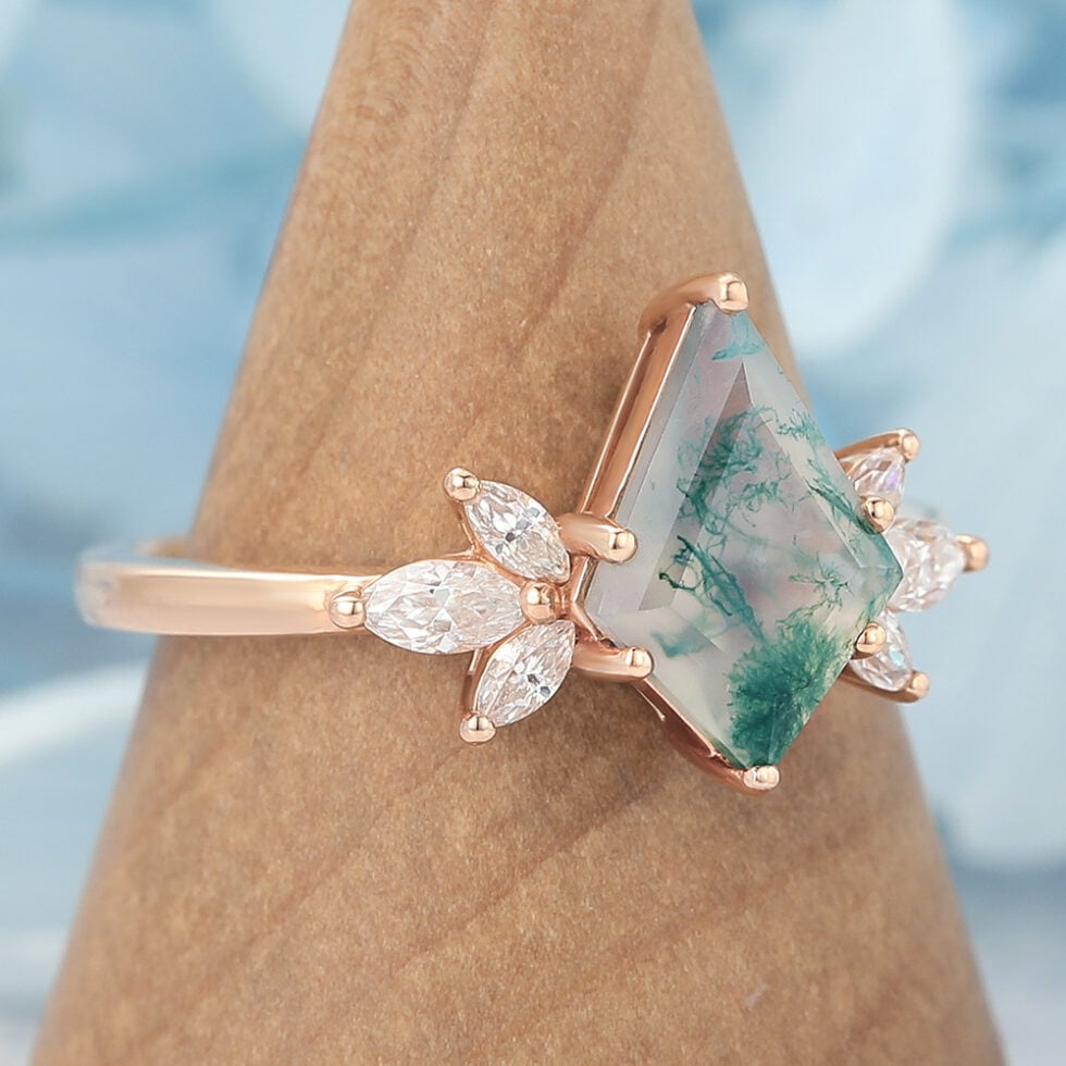 This nature-inspired engagement ring features a striking kite cut moss agate as the center stone, surrounded by a graceful cluster of marquise-cut accents that mimic the look of blooming petals or leaves. The rich, earthy patterns of moss agate make each ring truly one of a kind, while the marquise details add sparkle and movement.