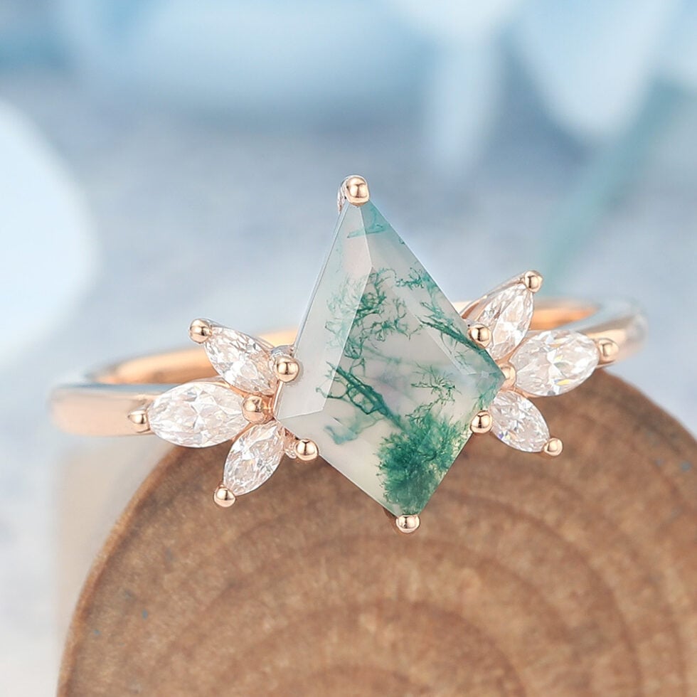 This nature-inspired engagement ring features a striking kite cut moss agate as the center stone, surrounded by a graceful cluster of marquise-cut accents that mimic the look of blooming petals or leaves. The rich, earthy patterns of moss agate make each ring truly one of a kind, while the marquise details add sparkle and movement.