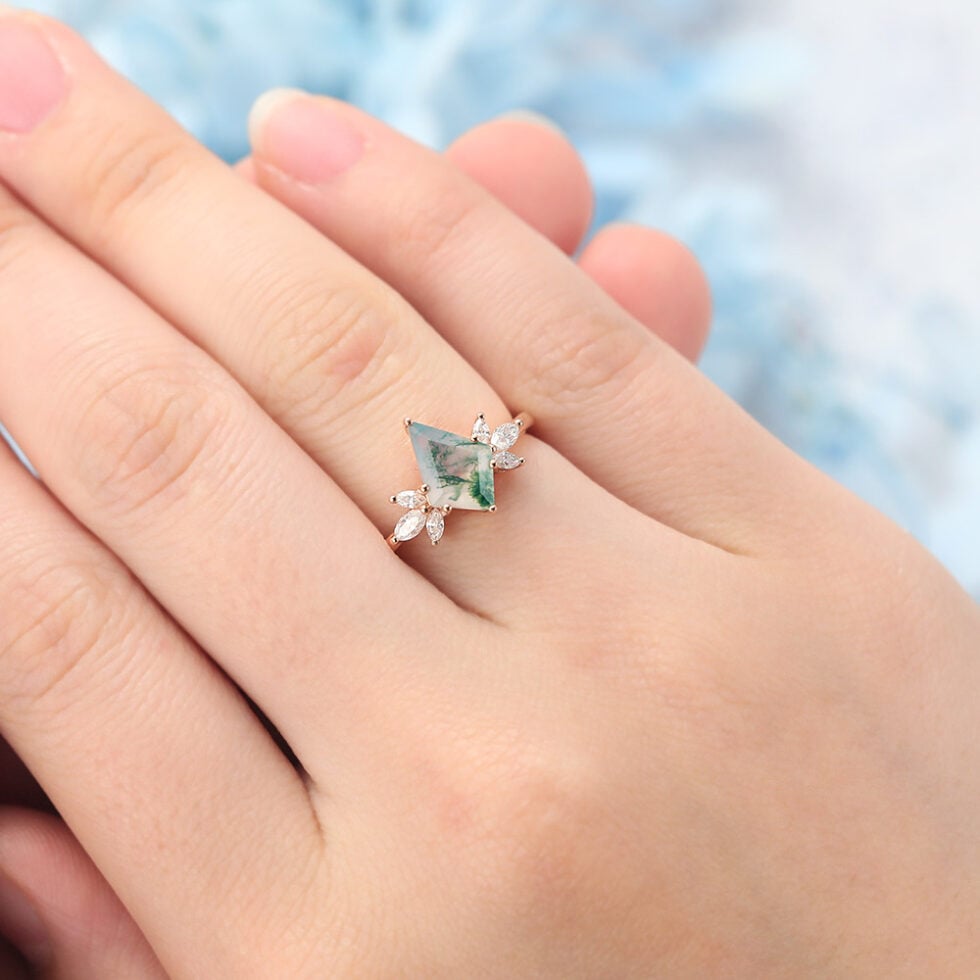 This nature-inspired engagement ring features a striking kite cut moss agate as the center stone, surrounded by a graceful cluster of marquise-cut accents that mimic the look of blooming petals or leaves. The rich, earthy patterns of moss agate make each ring truly one of a kind, while the marquise details add sparkle and movement.