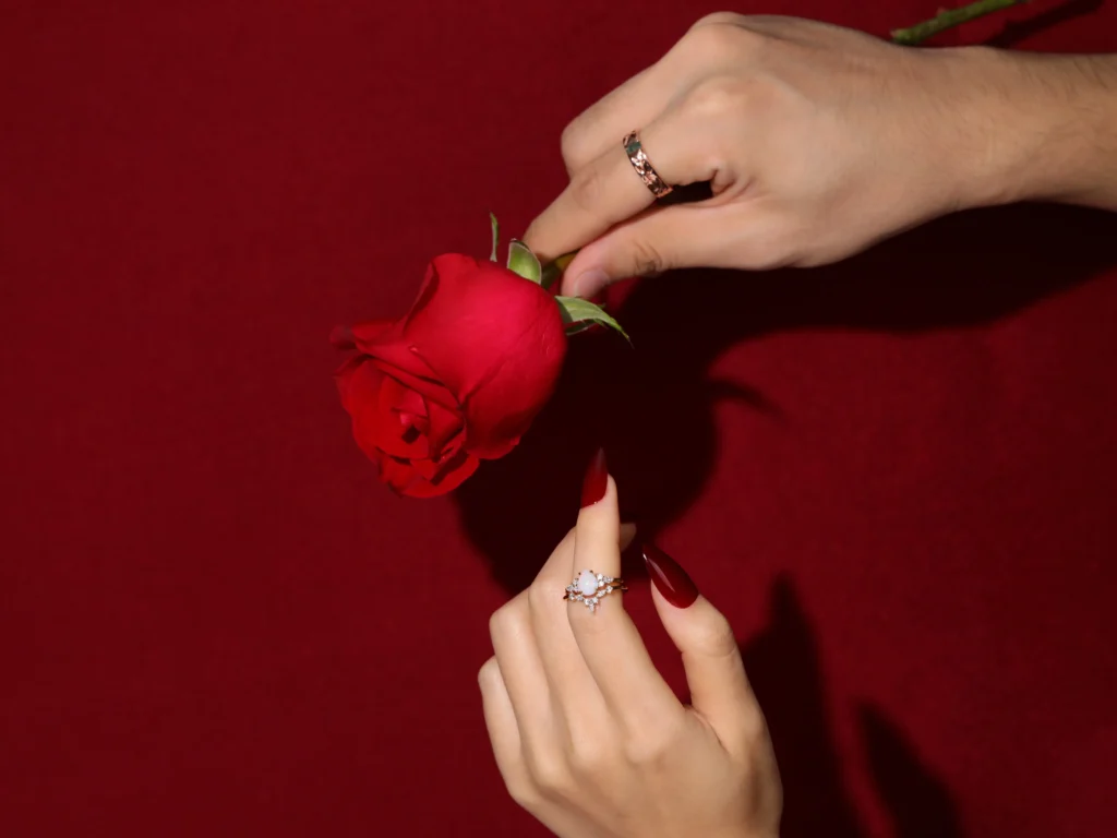 A romantic moment with a man handing a rose to a woman, showcasing the elegance of a men's straight band ring and a woman's opal stacking ring set, symbolizing love and commitment.
