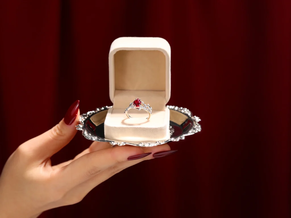 Elegant hand holding a silver tray with an open ring box, revealing a stunning ruby ring inside, symbolizing luxury and commitment